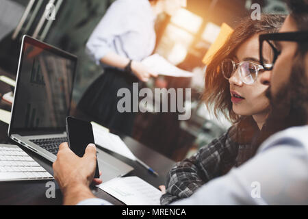 Group of creative coworkers working in modern loft space conducting brainstorming. Business team uses electronic device gadgets. Generic design notebo Stock Photo