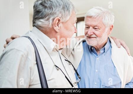 Two senior men in care home with arms around each other. Stock Photo