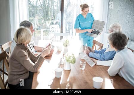 Care worker showing senior adults laptop in care home. Stock Photo