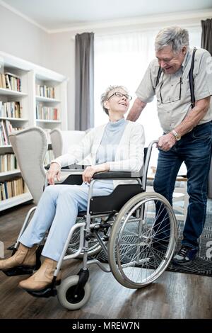 Senior woman in wheelchair looking at man and smiling. Stock Photo