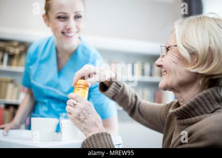 Care worker and senior woman opening medicine bottle. Stock Photo