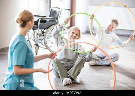 Physiotherapist with two senior women holding plastic hoops. Stock Photo