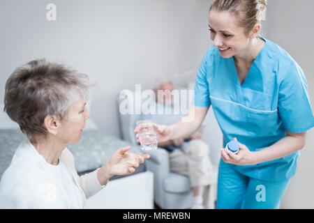 Care worker giving senior woman medication in care home. Stock Photo