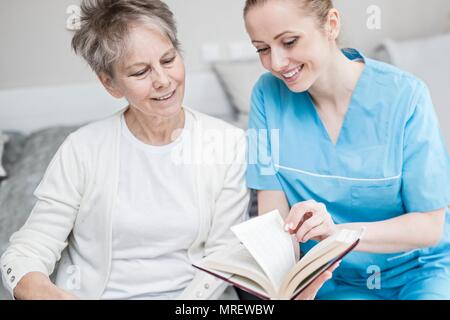 Care worker reading book with senior woman in care home. Stock Photo