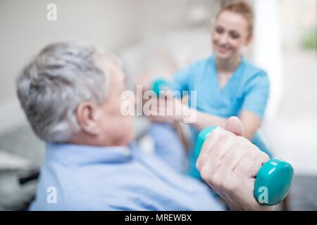 Senior man holding hand weight, physiotherapist helping. Stock Photo