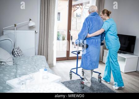 Care worker helping senior man to walk with a rollator. Stock Photo