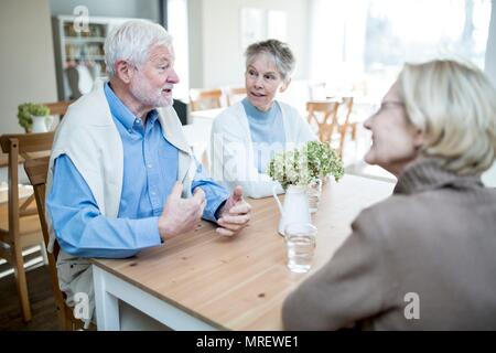 Senior man talking to two female friends in care home. Stock Photo