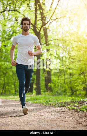 Young man is jogging in park. He is listening music on headphones. Stock Photo