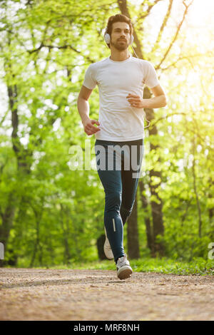 Young man is jogging in park. He is listening music on headphones. Stock Photo