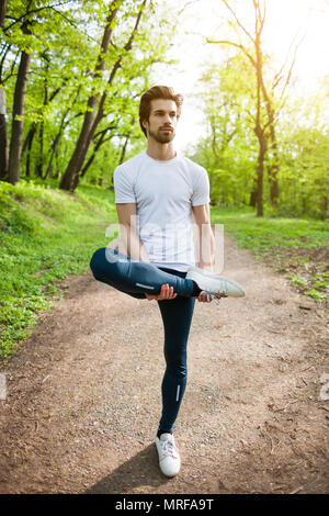 Young man is exercising in park. He is stretching his body. Stock Photo