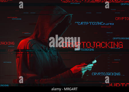 Cryptojacking scam concept with faceless hooded male person using tablet computer, low key red and blue lit image and digital glitch effect Stock Photo
