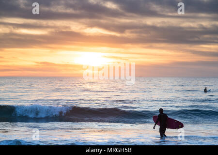 A longboard surfer walks into the ocean in Manhattan Beach, California on a cloudy day, ready to get a few waves before dark. Stock Photo