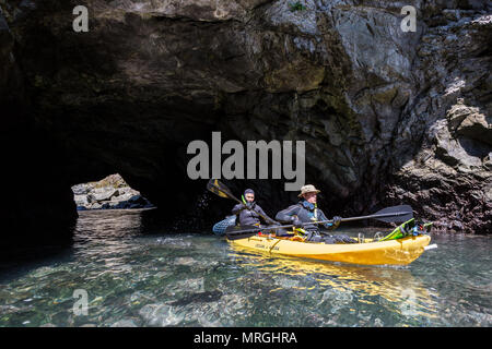 Two kayakers paddle through a sea arch near Russian Gulch State Park, clad in wetsuits for freediving. Stock Photo