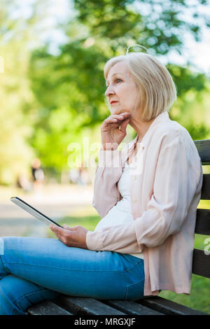 Adult woman sitting in park and using digital tablet. Stock Photo