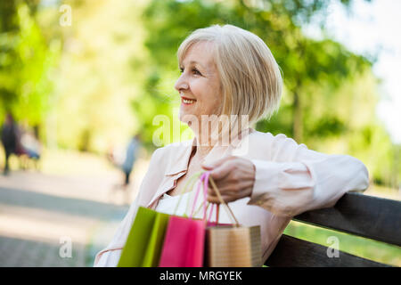 Happy adult woman sitting in park after shopping. Stock Photo