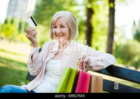Happy adult woman sitting in park after shopping. Stock Photo