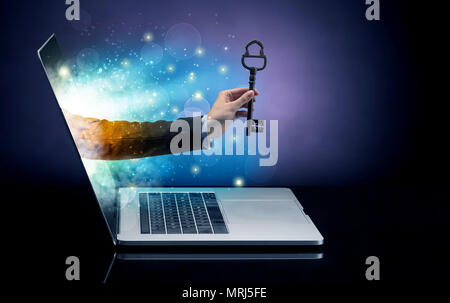 Hand with huge vintage key coming out of a laptop with sparkling effects  Stock Photo