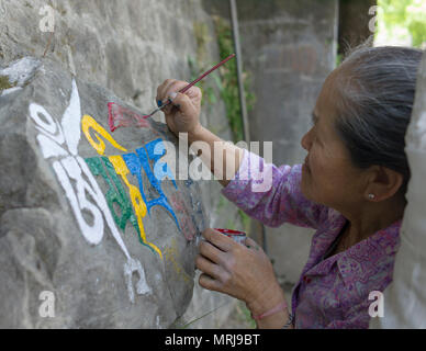 old Tibetan woman painting a mantra on a stone outside the Dalai Lamas temple in Macleodganj Dharamsala India. Stock Photo