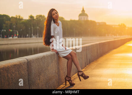 Young asian woman sitting on city stone quay at morning sunrise. Soft and beauty portrait. Stock Photo