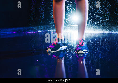 Woman legs with sports sneakers standing on water. Studio with rain and drops interior. Stock Photo