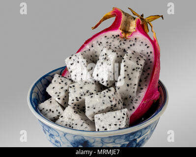 Dragon fruit cut in half in a blue bowl against a grey background Stock Photo