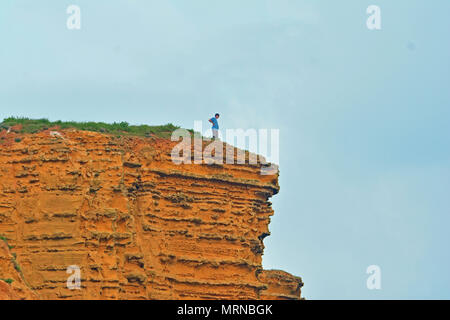 Dorset, UK. 26 May 2018. May Bank Holiday Weekend. Alone person stands on top of Dangerous Cliffs at West Bay in Dorset where in the past parts of the Famous cliff face have given way. Warning Signs have been put in place since stating the Dangers but still people put themselves at risk and others beneath. Robert Timoney/Alamy/Live/News