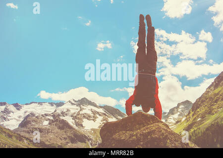 Practice gymnastic exercises in the open air in nature. Stuntman doing a dangerous trick on the edge of a precipice high in the mountains, handstand.  Stock Photo