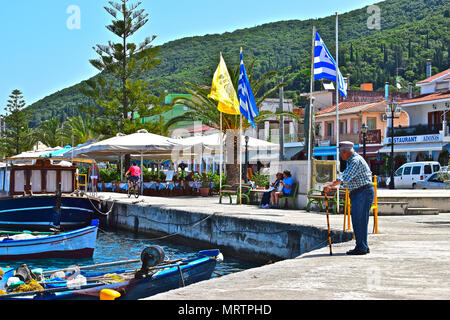 An old Greek man leans on his walking stick & looks across the harbour of the pretty port of Sami in Kephalonia / Cephalonia in Greece. Stock Photo