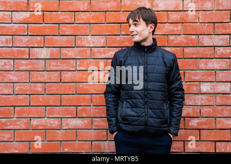 a young man stands leaning against a brick wall. Stock Photo