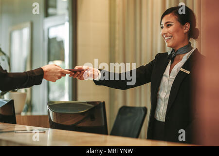 Smiling receptionist behind the hotel counter attending female guest. Concierge giving the documents to hotel guest. Stock Photo