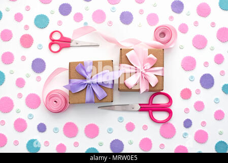 Two gift boxes on festive pastel confetti background. Wrapping gifts in Kraft boxes with a satin ribbon bow scissors. Flat lay top view Stock Photo