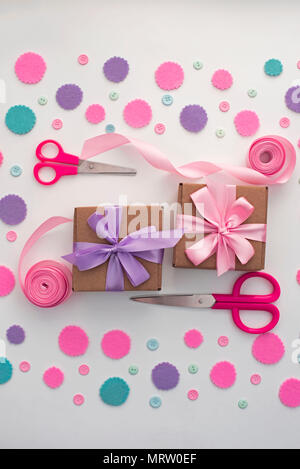 Two gift boxes on festive pastel confetti background. Wrapping gifts in Kraft boxes with a satin ribbon bow scissors. Flat lay top view Stock Photo