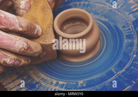 Potters hands shaping a bowl out of clay. Man cleans with sponge pottery on a Potter's wheel. The final stage of manufacture of the jug Stock Photo