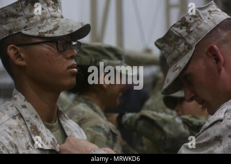 U.S. Marine Corps Staff Sgt. Brent Morris, the data chief with Special Purpose Marine Air-Ground Task Force-Crisis Response-Central Command, pins the air assault badge to the chest of Lance Cpl. Davy Yang, a cyber network operator with SPMAGTF-CR-CC, during a recognition ceremony while forward deployed in the Middle East, April 14, 2017. The air assault course is designed to teach servicemembers skills such as rappelling techniques and sling load procedures. SPMAGTF-CR-CC is a well-trained crisis response unit that has the ability to project combat power over vast distances using organic aviat Stock Photo