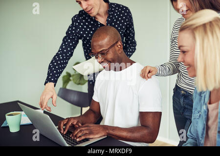 Diverse group of smiling businesspeople working together online with a laptop at a table in a modern office Stock Photo