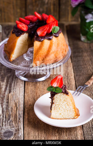 Homemade bundt cake with dark chocolate ganache glaze and fresh strawberries on top on rustic wooden table Stock Photo