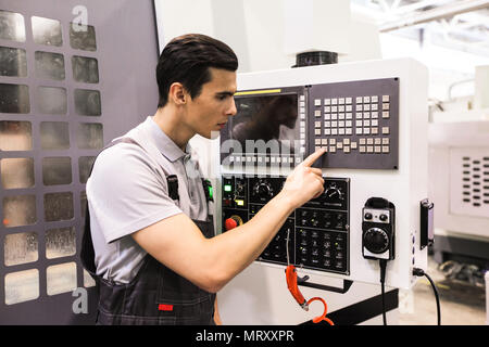 Worker pressing programming buttons on CNC machine control board in factory Stock Photo