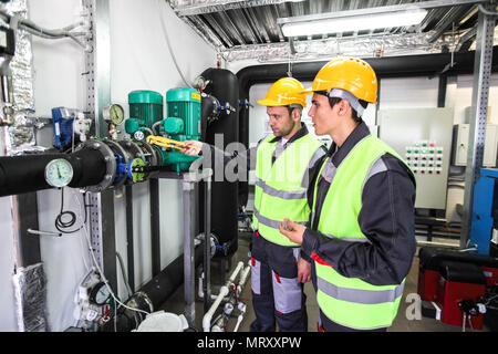 Two workers in hardhats at plant checking parameters of pressure Stock Photo