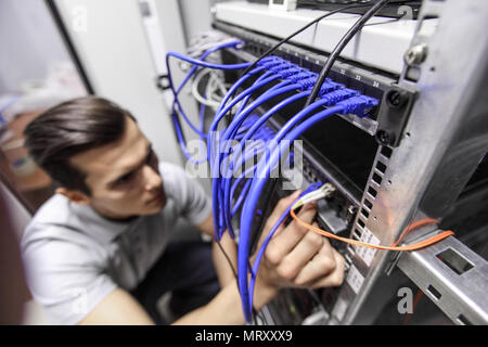 Young engeneer man in network server room connecting wires and checking rack devices Stock Photo