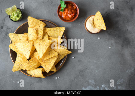 Nachos chips and various dip sauces. Tortilla corn nachos chips with salsa, melted cheese and guacamole, mexican snacks. Stock Photo