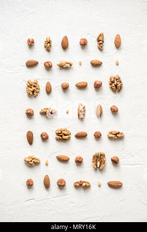 Various nuts (walnuts, hazelnuts, almonds and pine nuts) on white background as pattern, flat lay with copy space. Stock Photo
