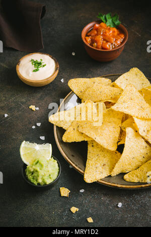 Nachos chips and various dip sauces. Tortilla corn nachos chips with salsa, melted cheese and guacamole, mexican snacks. Stock Photo