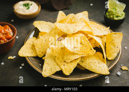 Nachos chips and various dip sauces, close up. Tortilla corn nachos chips with salsa, melted cheese and guacamole, mexican snacks. Stock Photo