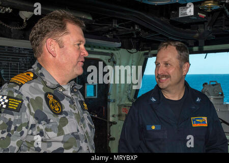 170714-N-DL434-031 CORAL SEA (July 14, 2017) Capt. Larry McCullen (right), commanding officer of the amphibious assault ship USS Bonhomme Richard (LHD 6), speaks with Royal Australian Navy Capt. Guy Holthouse, Sea Combat Commander for the Talisman Saber 2017 Combined Amphibious Force, on the ship’s bridge during Talisman Saber 17. Bonhomme Richard, part of a combined U.S.-Australia-New Zealand expeditionary strike group, is undergoing a series of scenarios that will increase naval proficiencies in operating against blue-water adversarial threats and in its primary mission of launching Marine f Stock Photo