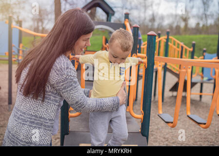 Closeup portrait of a happy mother and son playing on playground and having fun. Young mother playing with her baby boy outside in park. Mom and son. Stock Photo