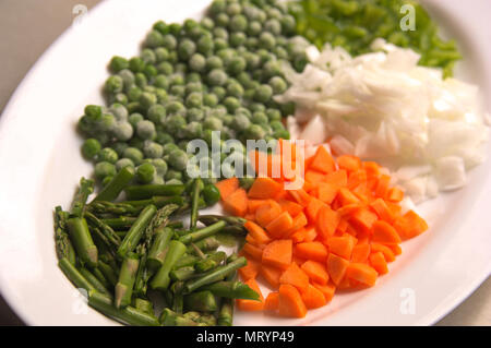 View of a plate with freshly cut vegetables. Carrot, onion, wild asparagus and green pepper. Stock Photo