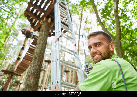 Young man stands in front of the ladder in the high ropes course at the teambuilding event Stock Photo