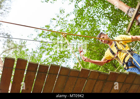 Young man carefully walks over a bridge in the high wire garden or climbing forest Stock Photo