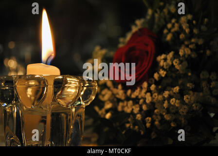 Decoration of a white candle lighting a bouquet of flowers with a white rose in the background Stock Photo