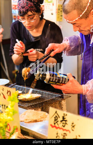Indoor Omicho Ichiba, Omicho fresh food Market in Kanazawa, Japan. Take away seafood food stall with mature man cooking scallops with blowtorch. Stock Photo